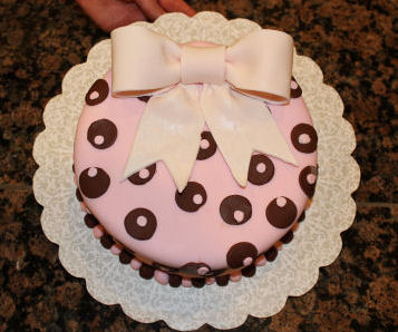 3 Layer round pink and brown baby shower cake decorated with pink and brown polka dots and a light pink gum paste bow