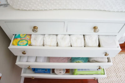 The white nursery dresser drawers are filled with baby girl outfits diapers and changing needs